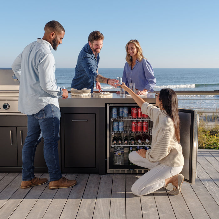 Couple grilling at a Stono outdoor kitchen island with ocean waves in the background, showing the grill, counter run and storage as one unit.