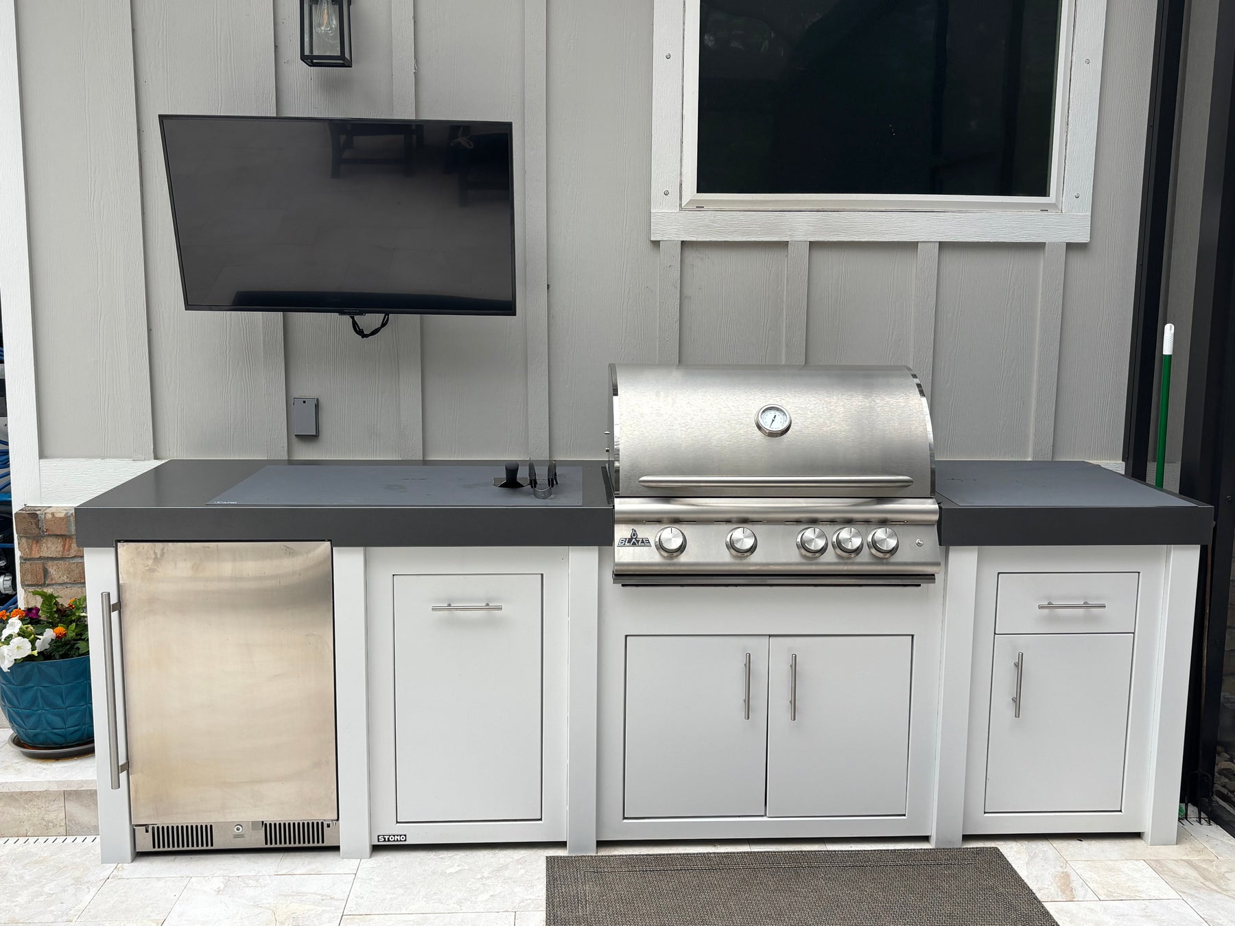 Stono engineered outdoor kitchen island with a built-in stainless grill and storage cabinets on a stone patio.