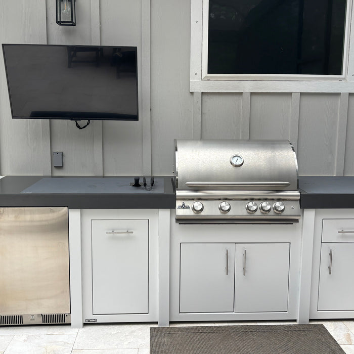 Stono engineered outdoor kitchen island with a built-in stainless grill and storage cabinets on a stone patio.