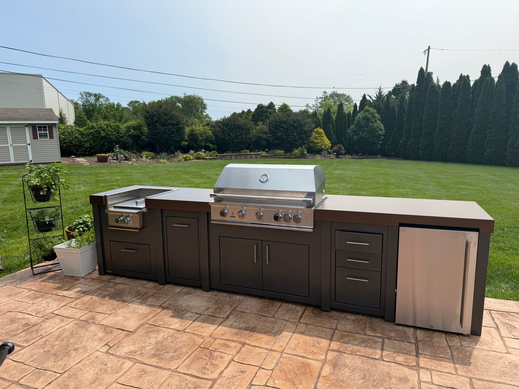 A Stono engineered outdoor kitchen with a built-in stainless grill and storage cabinets on an open patio, exposed to the weather.
