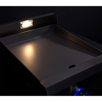 Stono Outdoor Living A close-up of the Le Griddle Pro Series 40 (OML40P3) 1 Burner Gas Griddle shows an interior light illuminating the stainless steel cooktop, with a blue-lit control knob visible against a dark background.