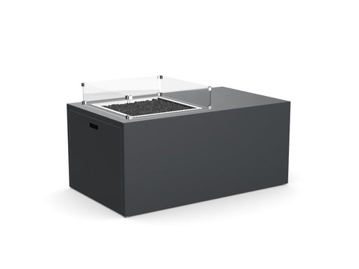 Stono Outdoor Living The Stono Outdoor Living Milan Offset is a modern rectangular fire pit table in dark gray, with a glass wind guard and black stones around the burner, shown against a plain white background.